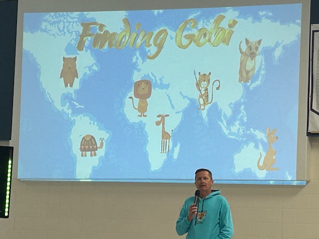Author Dion Leonard presenting on his book Finding Gobi in front of a blue screen with animals and continents